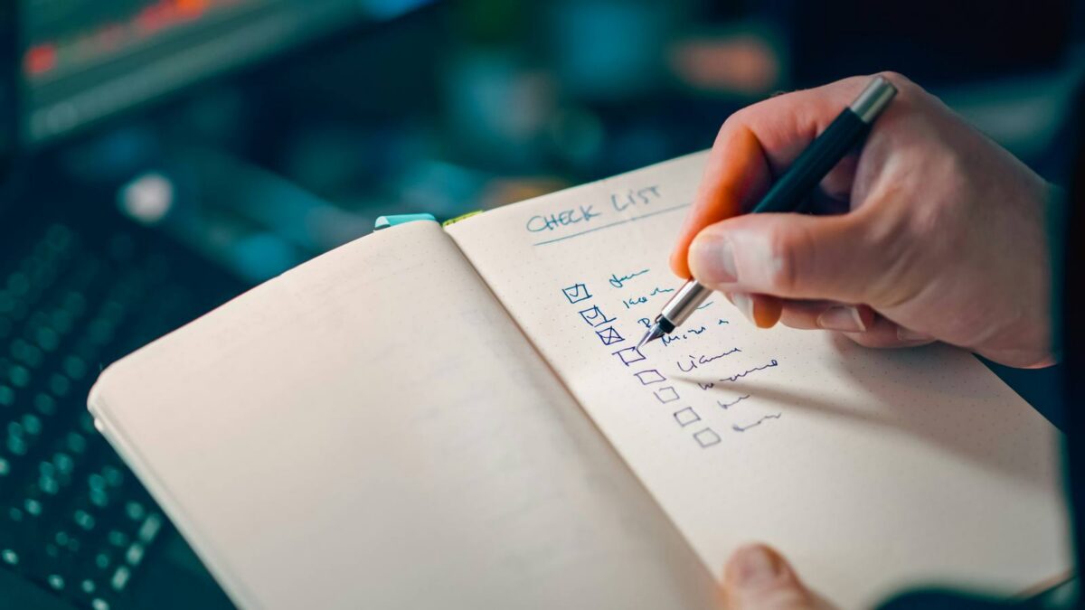 A hand checking a handwritten list in a notebook.