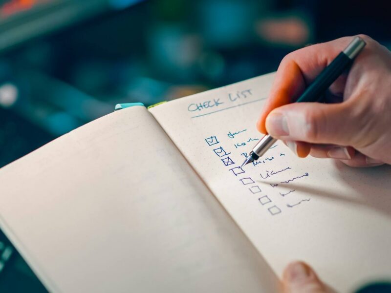 A hand checking a handwritten list in a notebook.
